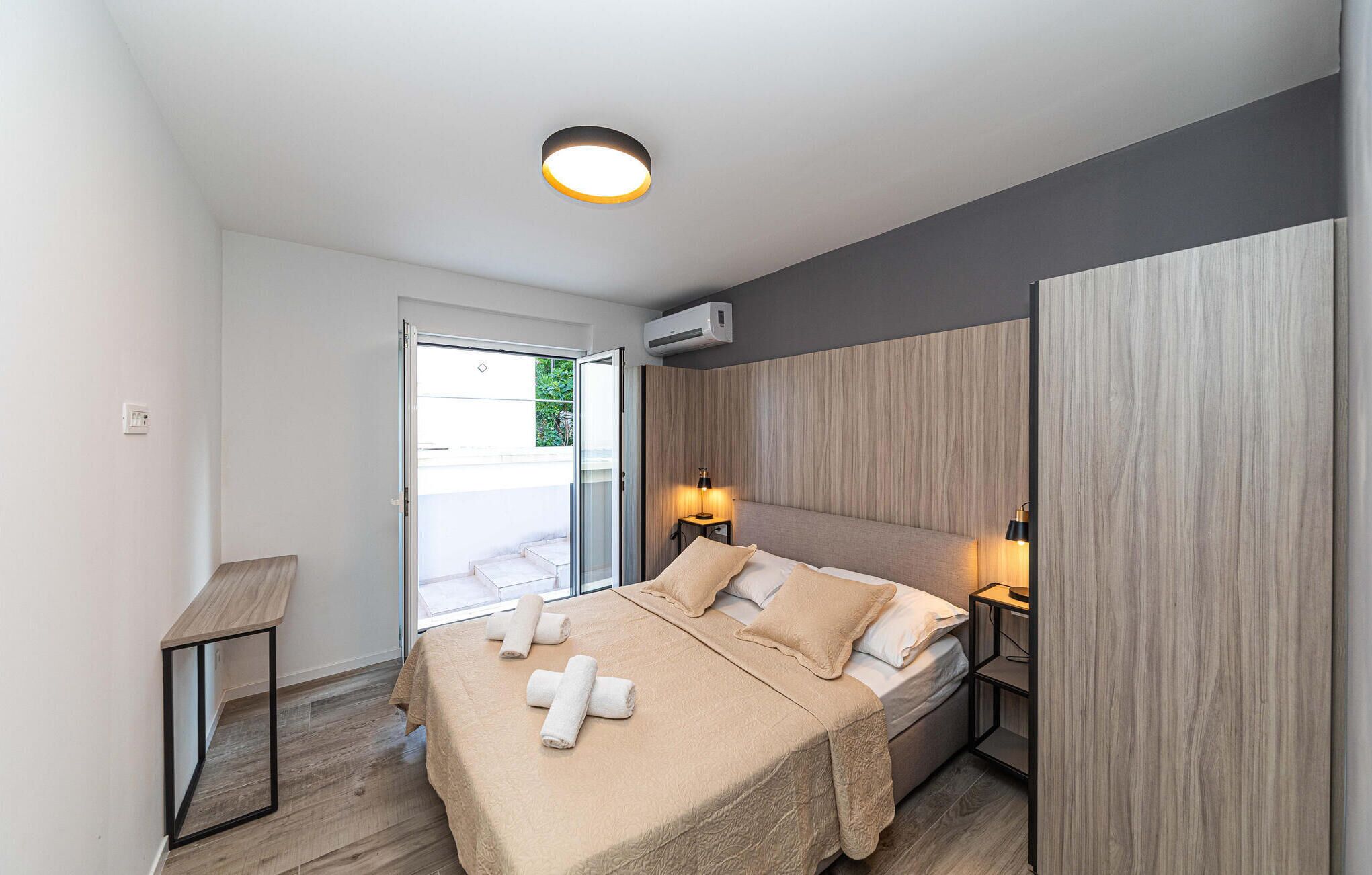 A modern bedroom with a bed, bedside lamps, a mirror, and an air conditioning unit.