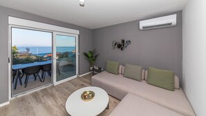 Una sala moderna con un sofá gris, una mesa de centro redonda y vistas al mar a través de un ventanal corredero.