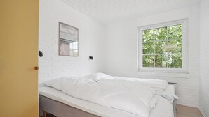Een kamer met witte bakstenen, een bed, een raam met uitzicht op bomen en een lijst met een afbeelding aan de muur.