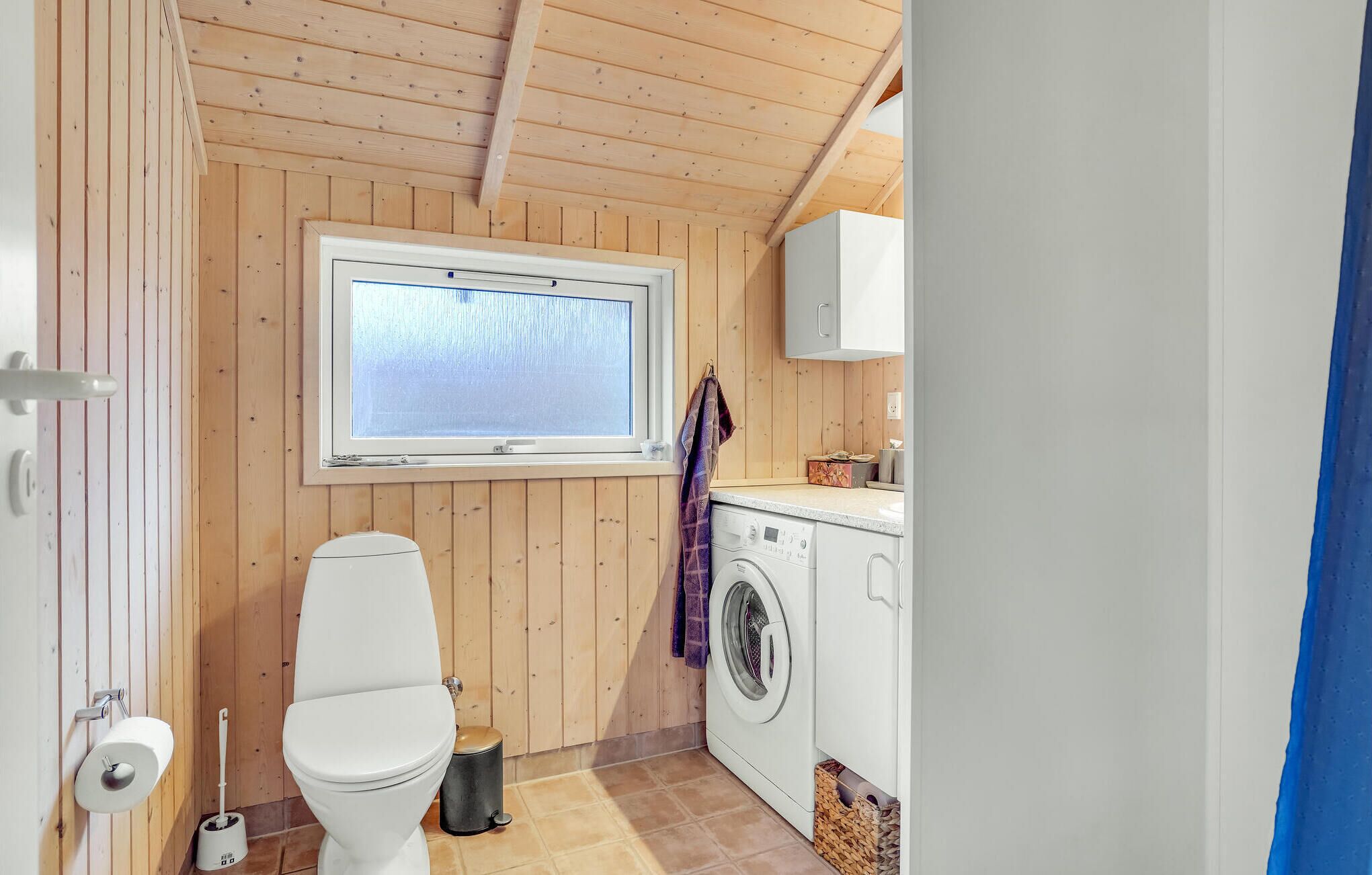 A compact bathroom with a toilet, washing machine, and a window.