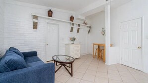Een woonkamer met een blauwe bank, een glazen salontafel en een witte wand met planken waarop decoratieve objecten staan.