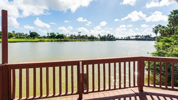 A wooden deck with a railing overlooking a calm lake, surrounded by greenery and trees. - Cheerful 2 Bedroom Cottage with fishing deck! (Bayview)