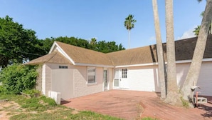 A single-story house with a brick exterior, a tiled roof, and a small front yard with grass and a red brick patio. - Cheerful 2 Bedroom Cottage with fishing deck! (Bayview)