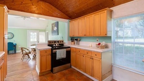 A kitchen with wooden cabinets, a stove, and a window with blinds. - Cheerful 2 Bedroom Cottage with fishing deck! (Bayview)