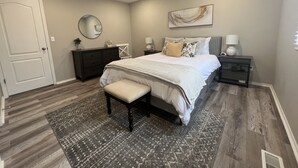 Een slaapkamer met een bed, nachtkastje, dressoir, plafondventilator, spiegel en een deur.