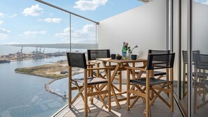 Ein Balkon mit Holztisch und -stühlen, mit Blick auf einen Hafen mit Schiffen und Kränen.