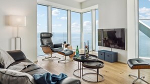Ein modernes Wohnzimmer mit gro ßem Fenster, einem Sofa, einem Sessel, einem Couchtisch und einem Fernseher.