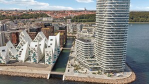 Ein modernes Hochhaus mit einem einzigartigen, geschwungenen Design, gelegen in der Nähe eines Ufers mit felsigem Uferhang.