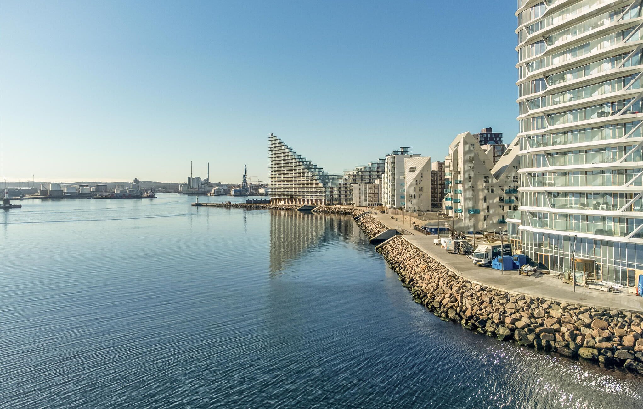 A waterfront hotel with modern architecture, a rocky breakwater, and a calm sea.