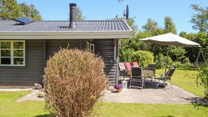 Une maison avec une cheminée, une antenne parabolique et une terrasse aménagée avec du mobilier d’extérieur.