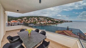 Un balcón con mesa y sillas, con vista a un pueblo costero con casas y al mar.