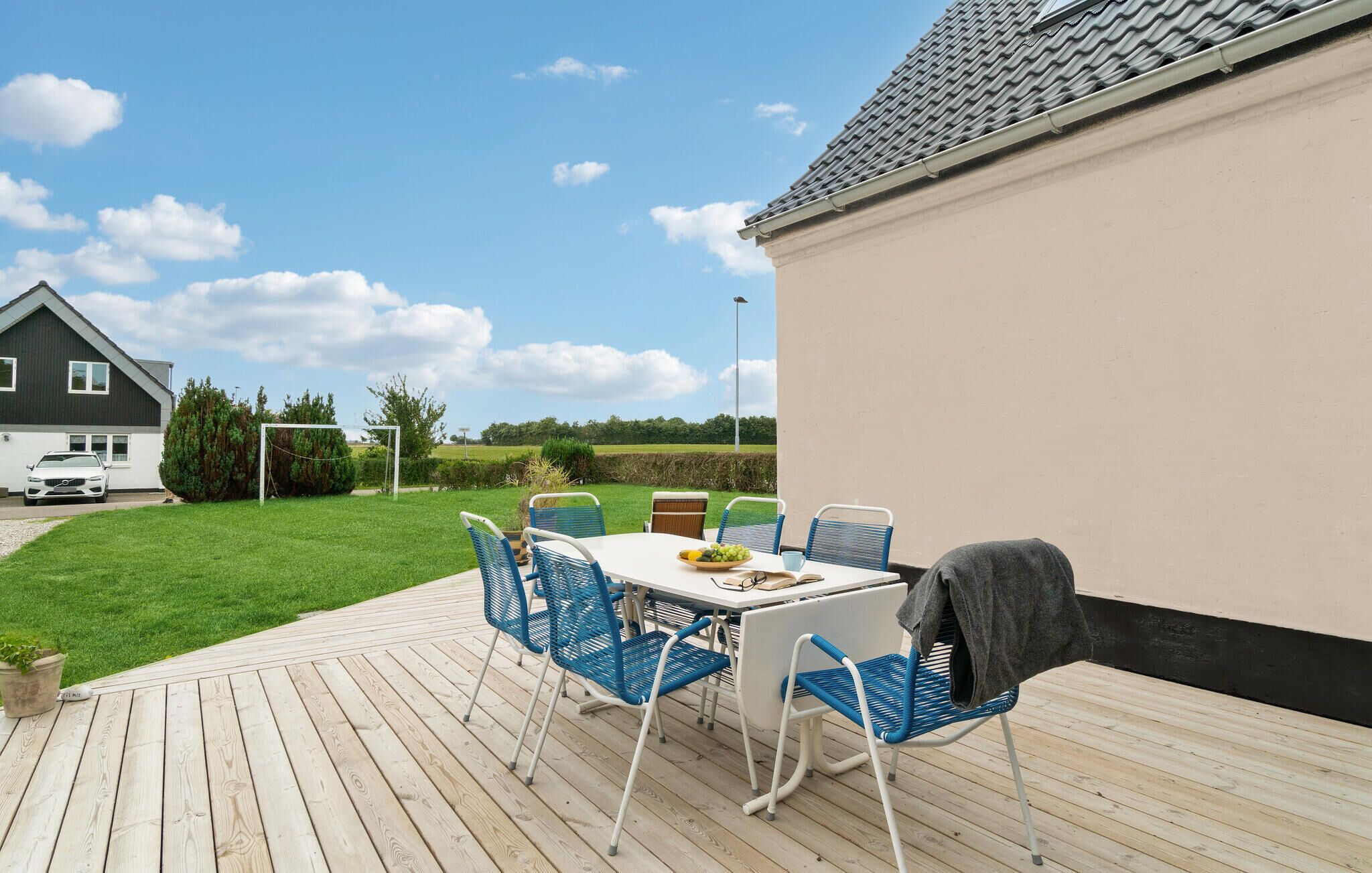 A wooden deck with a table and chairs, a white car parked in the driveway, and a house in the background.