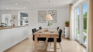 A modern kitchen with a wooden island, a dining area with a wooden table and black chairs, and a large window with a view of greenery. - 3 bedroom stunning home in Samsø (Samsø)