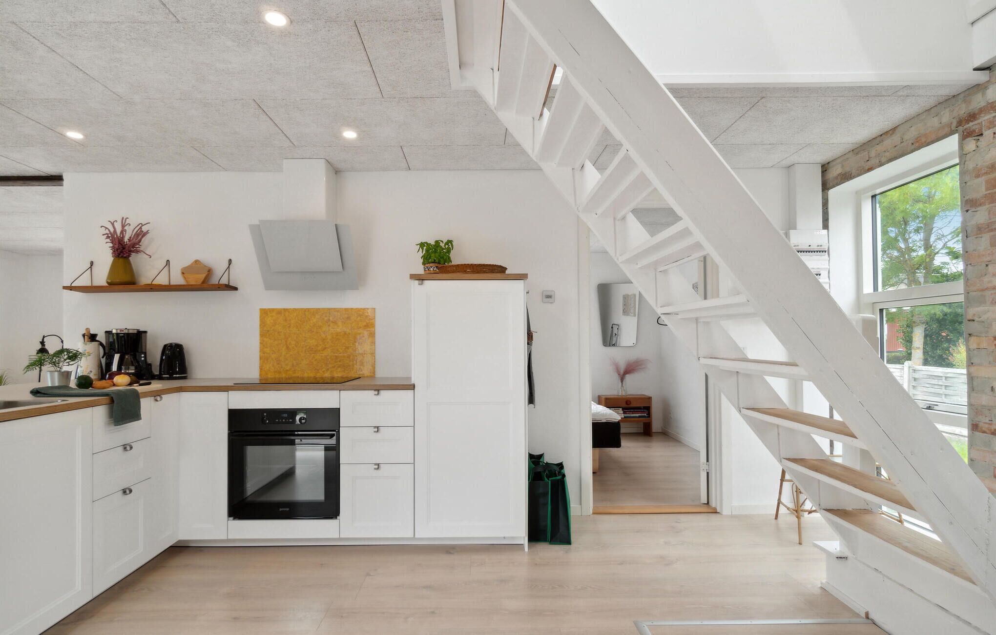 Een moderne keuken met witte kastjes, een ingebouwde oven en een houten aanrecht. Er is een trap met witte leuningen die naar een ander niveau leidt.