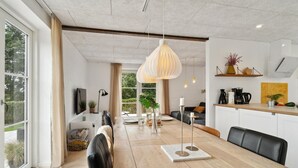 A modern kitchen with a dining area, large windows, and a view of greenery. - 3 bedroom stunning home in Samsø (Samsø)
