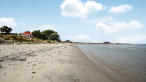 A sandy beach with a few buildings in the background, including a red-roofed house and a red barn. - 3 bedroom stunning home in Samsø (Samsø)