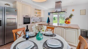 Una cocina moderna con armarios blancos, un refrigerador de acero inoxidable, un horno y un amplio ventanal con vista a un jardín.