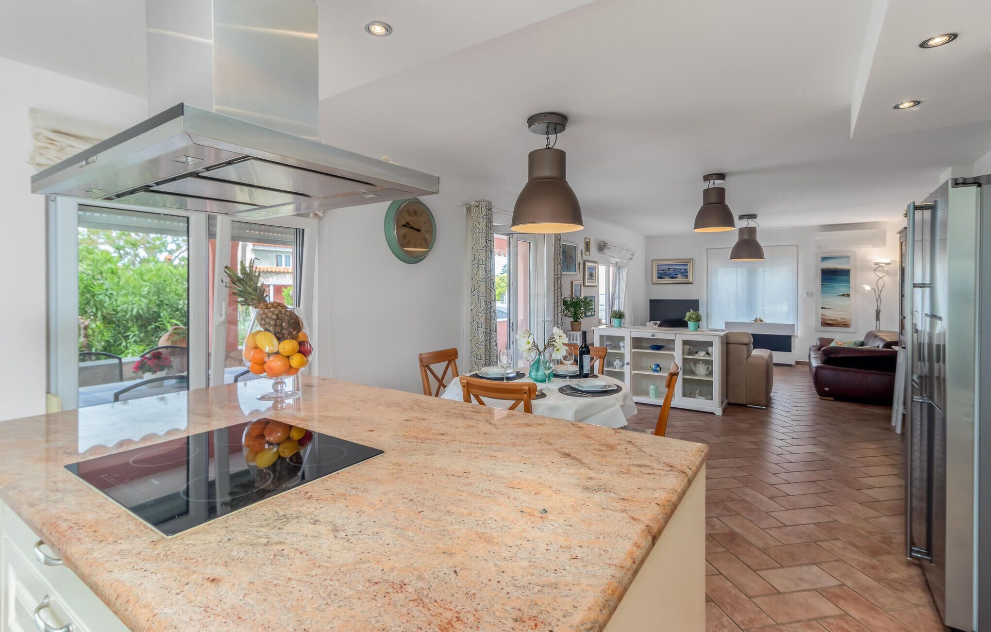 A modern kitchen with a central island, a dining area with a table and chairs, and a living area with a sofa and TV.