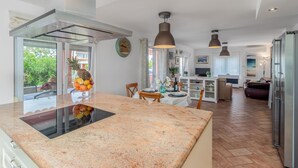 Una cocina moderna con una isla central, un comedor con mesa y sillas, y una sala de estar con sofá y televisor.