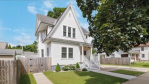 A two-story house with a front porch, a wooden fence, and a well-maintained lawn. - Vintage Home in Portage, WI (Portage)