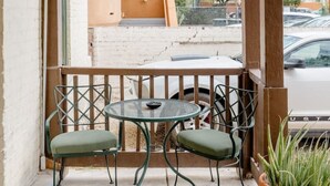 A covered outdoor seating area with a table and chairs, a potted plant, and a view of a building and street. - Charming 1BR Basecamp | Close to UofA (Tucson)