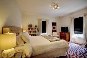 A bedroom with a large bed, a bedside lamp, a bookshelf, a dresser, and a television. - Walk to Downtown: Pet-Friendly Millerton Home! (Millerton)