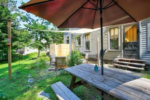 A wooden picnic table with benches, a large umbrella, and a grill area in a backyard. - Walk to Downtown: Pet-Friendly Millerton Home! (Millerton)