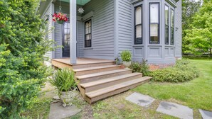 Een huis met een veranda, trappen die naar de ingang leiden, en een kleine tuin met plantenpotten.