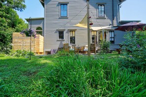 A two-story house with a front porch, a wooden fence, and a garden area with tall grass and flowers. - Walk to Downtown: Pet-Friendly Millerton Home! (Millerton)