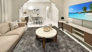 Una sala de estar moderna con sofá, mesa de centro y televisor. Se ve un comedor con una mesa y sillas al fondo.