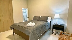 Un dormitorio con cama, mesita de noche, lámpara y una silla de madera.