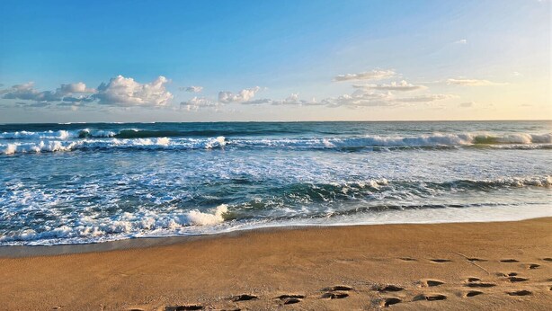 Una playa con olas, huellas y cielo despejado.