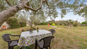 Een terras met een eettafel gedekt voor twee personen, omringd door stoelen, onder een boom.