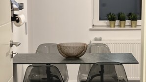 Un espace repas moderne avec une table en verre, des chaises transparentes et un centre de table composé d’un bol tressé.