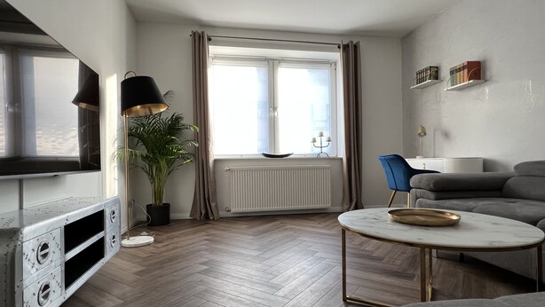Un salon moderne avec une télévision, une plante en pot, une table basse ronde et un canapé gris.