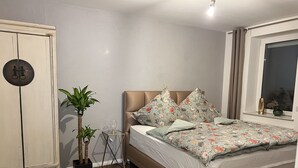 Une chambre à coucher avec un lit, une armoire, une plante en pot et une fenêtre avec des rideaux.