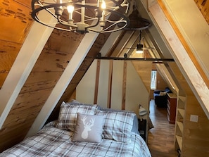 Une chambre confortable située dans les combles, avec un lit, un lustre et des poutres en bois.