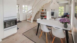 A modern kitchen with white cabinets, a built-in oven, and a staircase leading to a dining area with a white table and chairs. - Cozy apartment in Samsø with kitchen (Samsø)