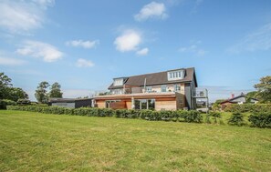 Une maison moderne à deux étages, dotée d’une grande pelouse à l’avant et d’un espace extérieur aménagé avec des sièges.