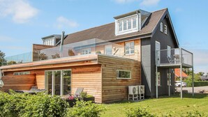 A modern two-story house with a balcony, wooden deck, and outdoor seating area. - Cozy apartment in Samsø with kitchen (Samsø)