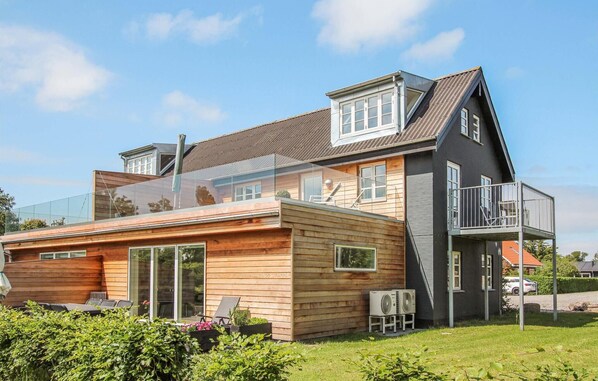 Une maison moderne à deux étages, dotée d’un balcon, d’une terrasse en bois et d’un espace salon extérieur.