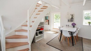 A modern interior with a spiral staircase, a dining area with a table and chairs, and a view through a window. - Cozy apartment in Samsø with kitchen (Samsø)