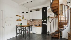 Cozinha moderna com ilha central, luminárias pendentes, escada em espiral e piso ladrilhado.