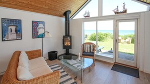 Uma sala de estar aconchegante com uma mesa de vidro, móveis de vime, lareira e vista para o mar.