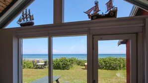 Quarto com grandes janelas que dão para uma área gramada e o oceano, com mesa de piquenique e modelo de navio.