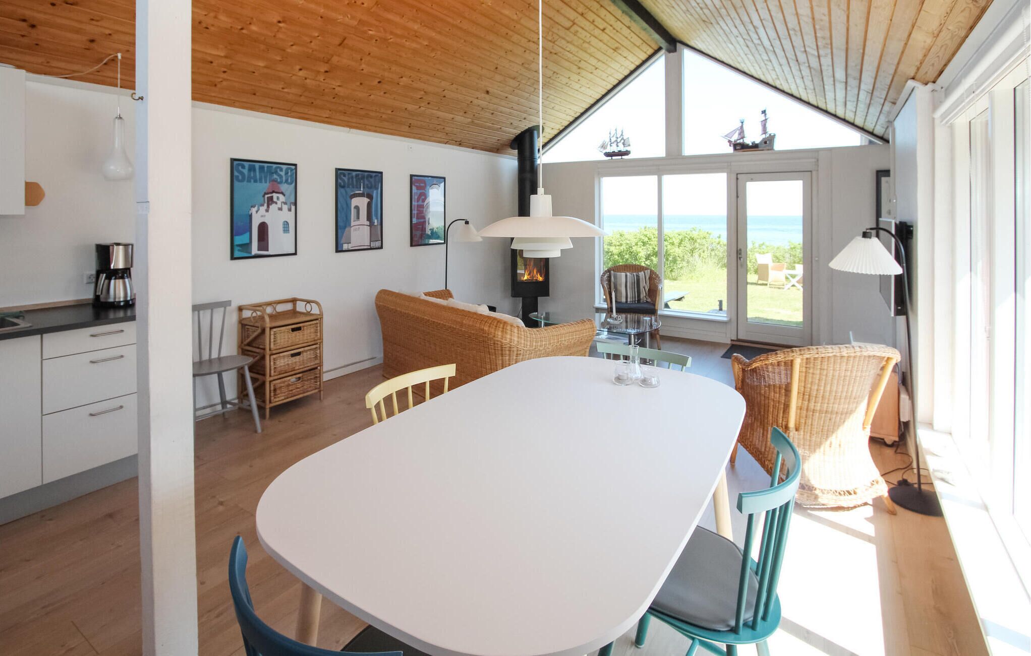 A modern kitchen with white cabinets, a dining table, wicker furniture, and a large window overlooking the sea.