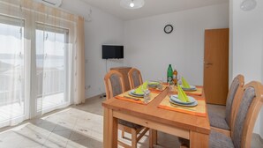 A dining area with a wooden table set for two, chairs, a television mounted on the wall, and a sliding glass door leading to a balcony. - Beautiful apartment in Ribarica (Ribarica)