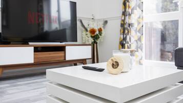 A modern living room with a flat-screen TV displaying 'NETFLIX', a remote control, and a candle on a white coffee table.