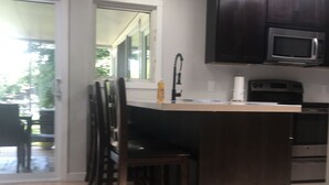 A kitchen with dark wooden cabinets, a microwave, and a built-in oven. There is a bar area with stools and a window overlooking a patio.