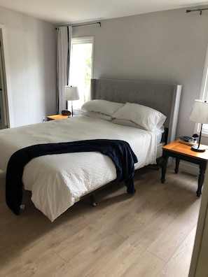 A bedroom with a large bed, a bedside table with a lamp, and a window with curtains. - Waterfront, Snowmobile trials nearby, close to town (Kawartha Lakes)